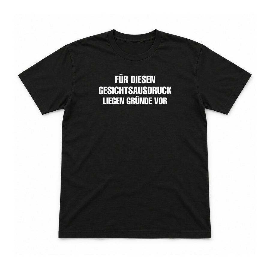 Für diesen Gesichtsausdruck liegen Gründe vor – Unisex T-Shirt – Black – Flat-Lay Vorderseite (Mockup)